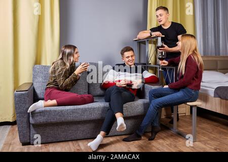 Two couples in love met in an apartment for a double romantic date. Young people communicate, they have glasses of wine in their hands. Men and women Stock Photo