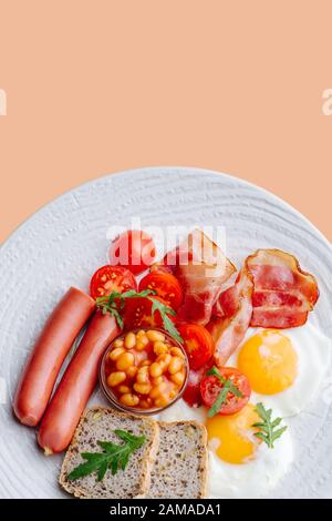 Hearty breakfast: fried eggs, bread, sausages, bacon, cherry tomatoes and beans. Stock Photo