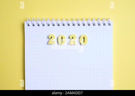 Wooden figures 2020 next to the notebook on a yellow background. Top view. Close up. Stock Photo