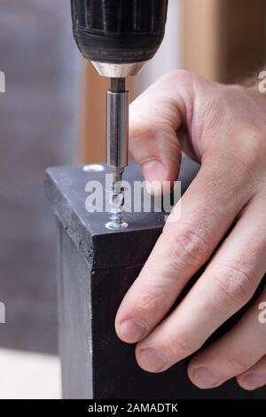 Side view and close up photo of carpenter person with professional electric screwdriver instrument in hand and repairing, fixing Stock Photo