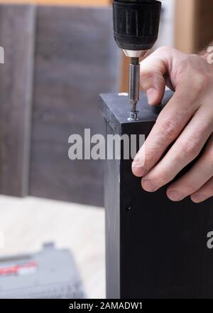 closeup man worker in work clothes working with screwdriver in his hands is assembling furniture. Stock Photo