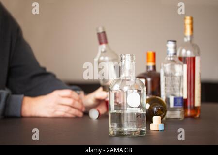 Man sitting lifting a bottle of alcohol and an empty glass by the side at a table in home or bar environment. Selective focus. Close up image Stock Photo
