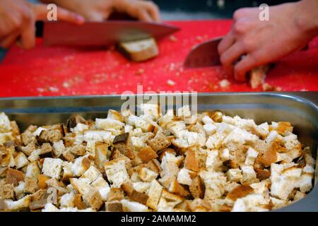 Man hands cutting bread for crutons on red cutting doard. Preparing bread for roasting croutons. Stock Photo