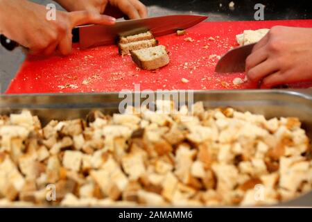 Man hands cutting bread for crutons on red cutting doard. Preparing bread for roasting croutons. Stock Photo
