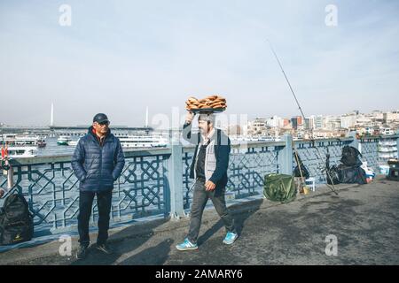 Turkey, Istanbul, December 29, 2019 - The seller walks along the Galata bridge and bears on his head many traditional Turkish bagels Simit. Street food business. Stock Photo