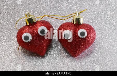 two large eyes on red glitter hearts on glittering silver glitter background Stock Photo