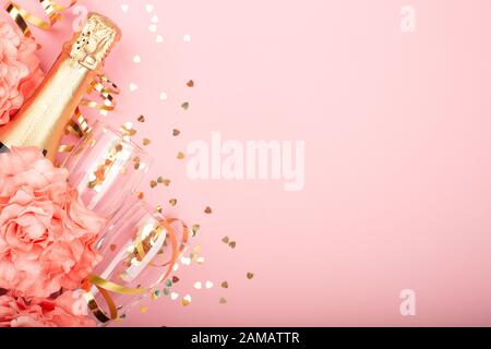 Valentines day champagne bottle flute glasses golden confetti hearts rose flowers and serpentine on pink background with copy space for text Stock Photo