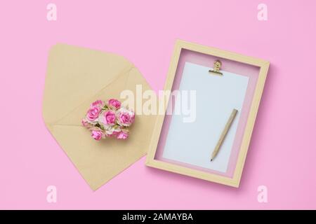 Mockup photo frame with kraft rose flower in brown envelope for Valentines day concept. Top view of mock up photo frame with craft decoration and on p Stock Photo