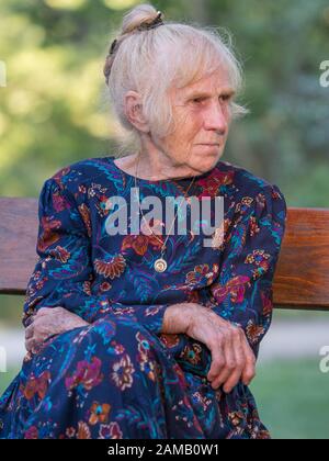 An elegantly dressed, elderly woman is sitting on a park benchis sitting on a park bench. Poland. Stock Photo