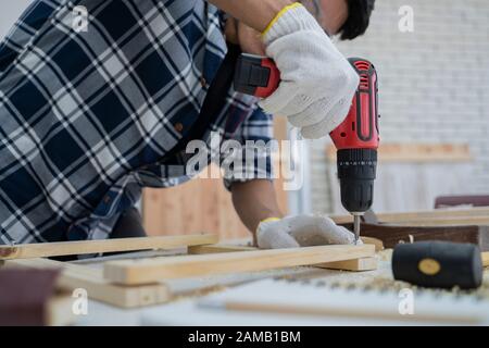 The carpenter is using an electric screwdriver to drill the workpiece. Stock Photo