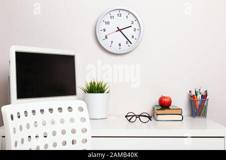 Student workplace. Closeup desk chair computer clock stack of books apple glasses stationery. Stock Photo