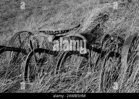 Old farm machinery abandoned at edge of field and in among grasses Stock Photo