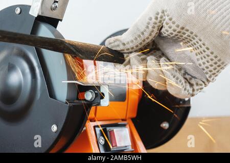 Sharpening the blade of a lawn mower with an electric sharpener. Hands in work gloves hold and sharpen the blade. Stock Photo