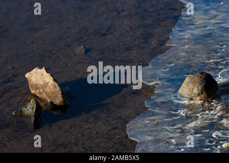 classic and minimal image of stone water and ice caught in close up and beautiful light with the sun highlighting both stones and ice Stock Photo