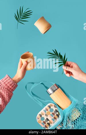Zero waste tea in in eco friendly insulated bamboo flask. Two hands with cup and palm leaf, net bag with lunch box and tea flask are flying. Zero wast Stock Photo