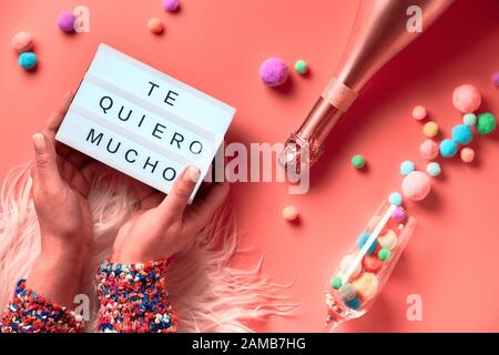 Text 'Te quero mucho' means I love you so much in English. Lightboard with text in Latino female hands, top view on pink background. Bottle of champag Stock Photo