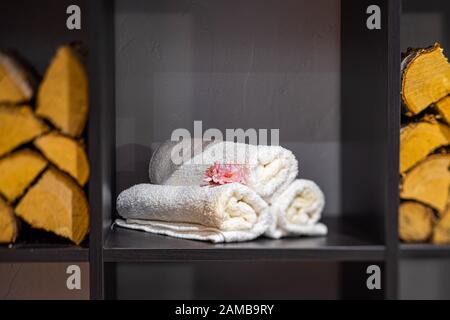 Rolled white towels on the black shelf. Rose flower. Close-up. Stock Photo