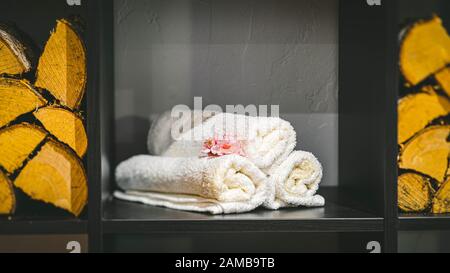 Rolled white towels on the black shelf. Rose flower. Close-up. Stock Photo