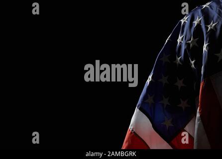 Back view of incognito holding american flag on shoulder. Crop of human with piece of fabric standing, posing in dark atmosphere. Concept of nation, patriotism. Stock Photo