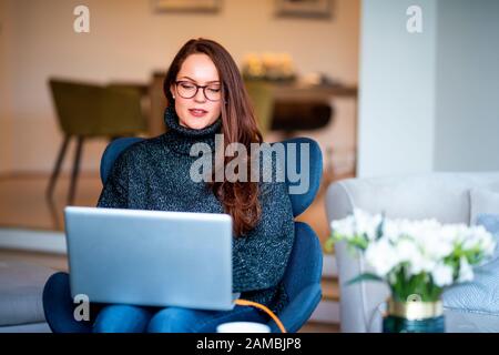 Shot of smiling young woman using her laptop while sitting on chair and working from home. Stock Photo