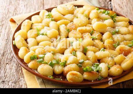 Vegetarian fried potato gnocchi with garlic, cheese and green onions close-up on a plate on the table. horizontal Stock Photo