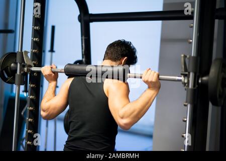 Bodybuilder doing squats using a squat cage in a gym to train his legs Stock Photo