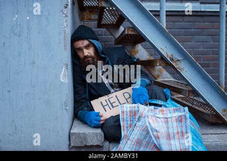 Bearded bum with help sign on city street Stock Photo