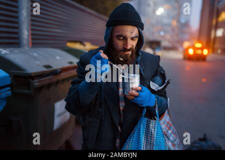 Homeless eating canned food on city street Stock Photo
