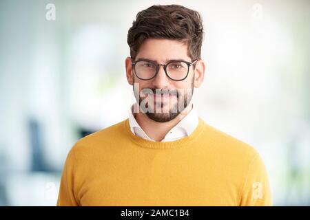 Portrait of smiling young man wearing glasses and sweater looking at camera and smiling. Stock Photo