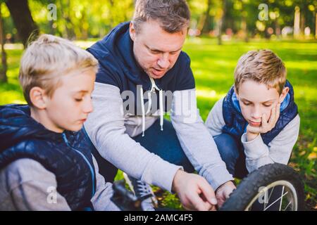 Father day. A large friendly family father and sons together actively relax in the fresh air. Dad teaches sons to repair bicycles. A child uses a tool Stock Photo