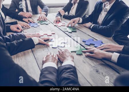 Businesspeople joining puzzle pieces on table, teamwork problem solution concept Stock Photo