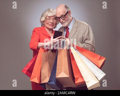 Happy elder couple with many shopping bags surfing the net online shopping concept Stock Photo