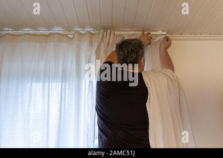 Hands of man installing curtains over window Stock Photo