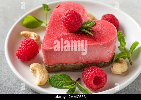 Valentines day dessert. heart shaped raw vegan red cake with raspberries and mint in a plate. healthy delicious food. close up. love concept Stock Photo