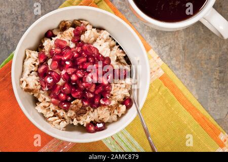 Hot oatmeal cereal topped with pomegranate seeds in white bowl with cup of black coffee. Stock Photo
