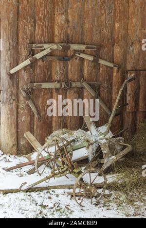 Snowy old gate and plowed plow leaning on a wooden log cabin in winter Stock Photo