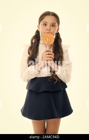 Sweets reward for study. Rewarding herself with sweets. Food addictions. Girl kid eat sweet lollipop. Girl pupil school uniform like sweets lollipop candy white background. Healthy nutrition diet. Stock Photo