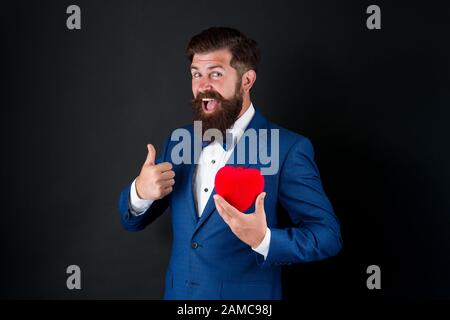 Fall in love. Celebrate love. Trust me. Happy valentines day. Tuxedo man hold red heart. Love concept. Passionate mature lover hipster in formal suit. Businessman with bow tie. Romantic greeting. Stock Photo