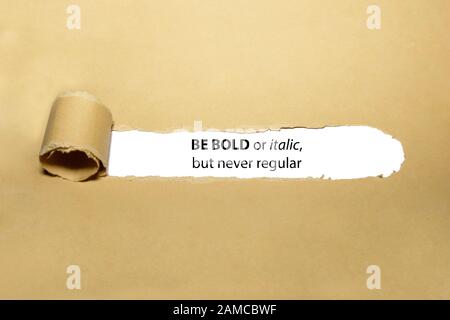 Inspirational quote Be Bold Or Italic But Never Regular appearing behind torn paper. Concept about the importance of being different and standing out Stock Photo