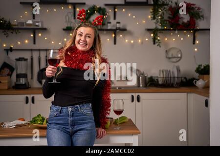 Happy woman with heart made from tinsel in hands standing in kitchen during Christmas. New Year celebration concept. Stock Photo