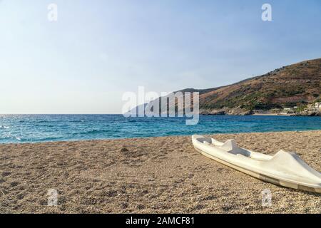Active rest, sport, kayak. Single white kayak stand on a stony beach on the seashore  of the Albanian Riviera. Stock Photo