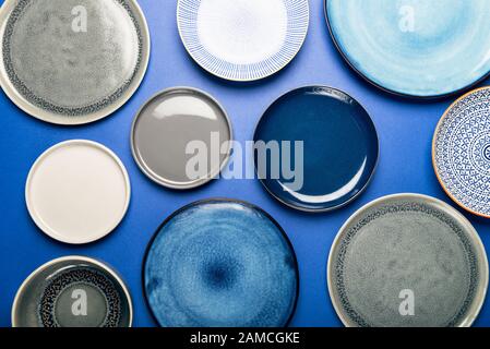 Different Ceramic Empty Blue and Grey Plates on Blue Background, Top View, Copy Space Stock Photo