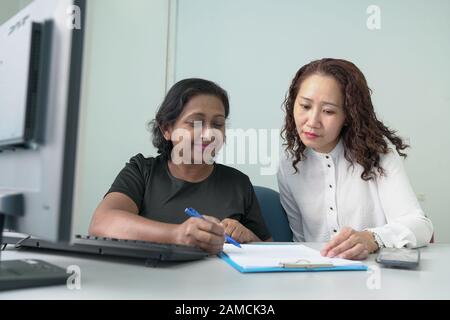 Two businesswomen or corporate professionals working together and in a discussion. Office table with computer. Stock Photo