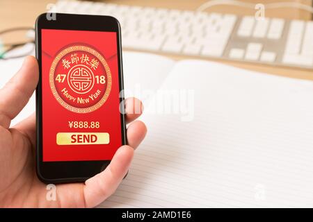 Hand holding smart phone with digital red packet for Chinese new year displayed on the screen -  holidays celebrations and technology concept. Stock Photo