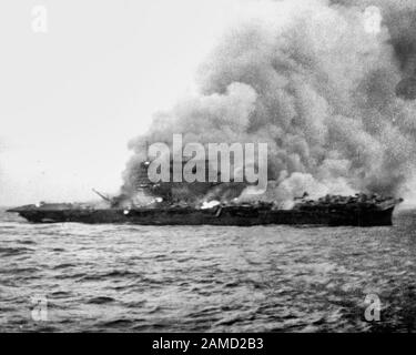 The U.S. Navy aircraft carrier USS Lexington (CV-2), burning and sinking after her crew abandoned ship during the Battle of the Coral Sea, 8 May 1942. Note the planes parked aft, where the fires have not yet reached. Stock Photo