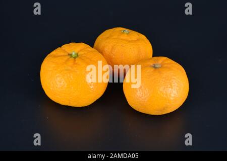 Juicy fruit, three small orange mandarins lies on a black plastic background. Delicious and sweet fruits, fruit vase, healthy food for every day. Stock Photo