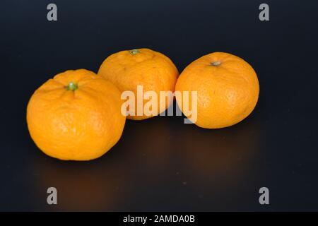 Juicy fruit, three small orange mandarins lies on a black plastic background. Delicious and sweet fruits, fruit vase, healthy food for every day. Stock Photo