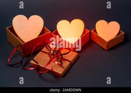 Three golden hearts in gift boxes on gray background. Red backlight Stock Photo