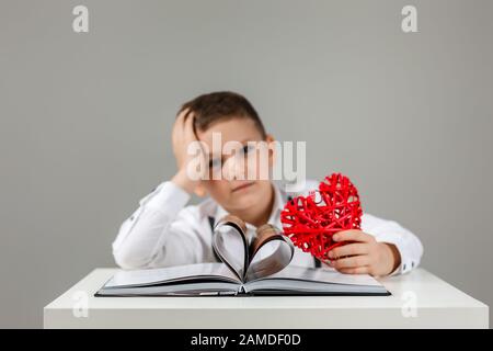 Portrait of cute child boy with red heart and book on gray background. valentine's day. Stock Photo
