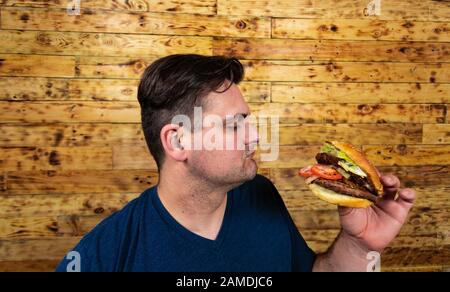 Young handsome man is posing with his tasty burger and about to enjoy it. Stock Photo